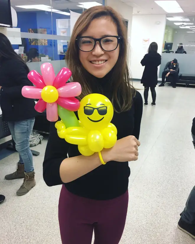 A smiling party guest holding a bright balloon flower and a yellow balloon creation
